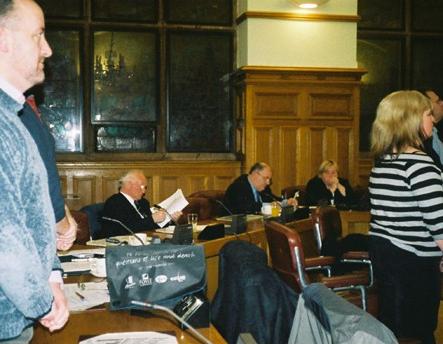 Inside the meeting Ernie Hamilton (UUP), Willie Hay (DUP) and Mildred Garfield (DUP) sit while the rest of the meeting stands for a minute's silence in honour of the victims of the arms trade.