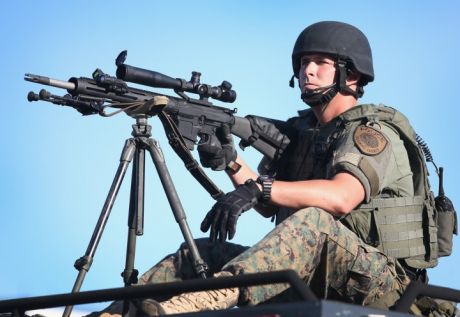 One of the heavily militarised police in Ferguson points his military sniper rifle at peaceful protesters