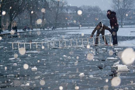 Ice skaters on the frozen lough put a ladder from the ice over water to the surrounding wall so that they can climb across and onto land