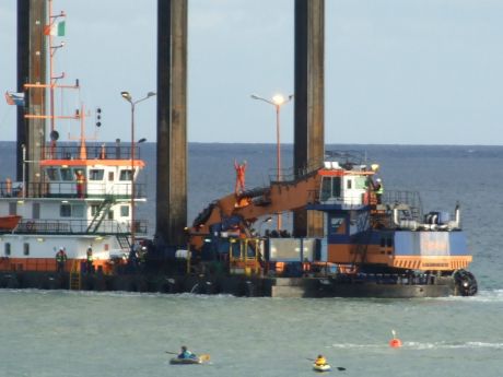 The dredger is being towed away by another vessel whilst protestor stands on digger.