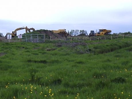 Diggers and dump trucks clearing topsoil and filling in monument remains
